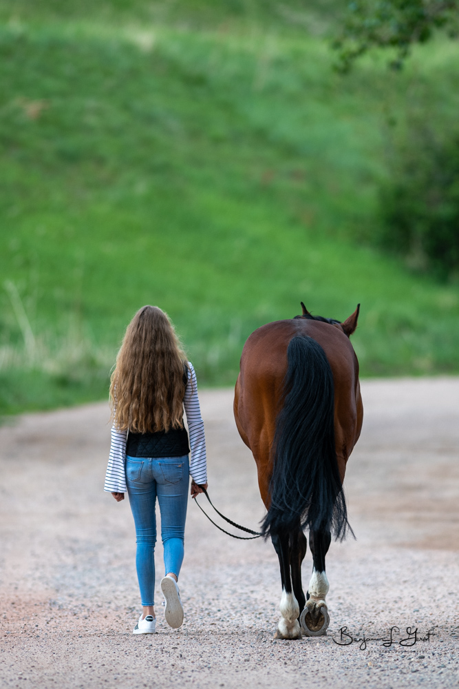 girl walks horse down dirt road